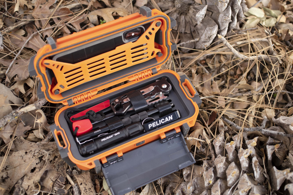 Orange R20 Ruck Case open to display storage compartment on lid, holding a mobile phone, and storage compartment in base, holding flashlights and utility knife.